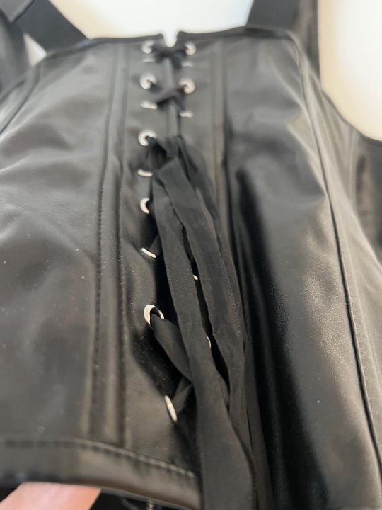 Corset i sort l&aelig;derlook med lynl&aring;s foran og sn&oslash;rre p&aring; ryg. Brystm&aring;l: 100-130 cm